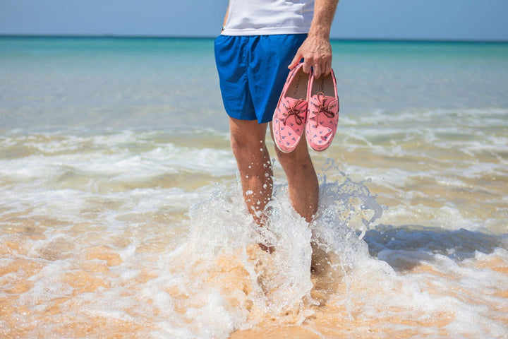 Man stands holding pink boat shoes in the ocean